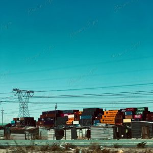 Shipping containers and industrial infrastructure rising behind a very different lived reality in the foreground